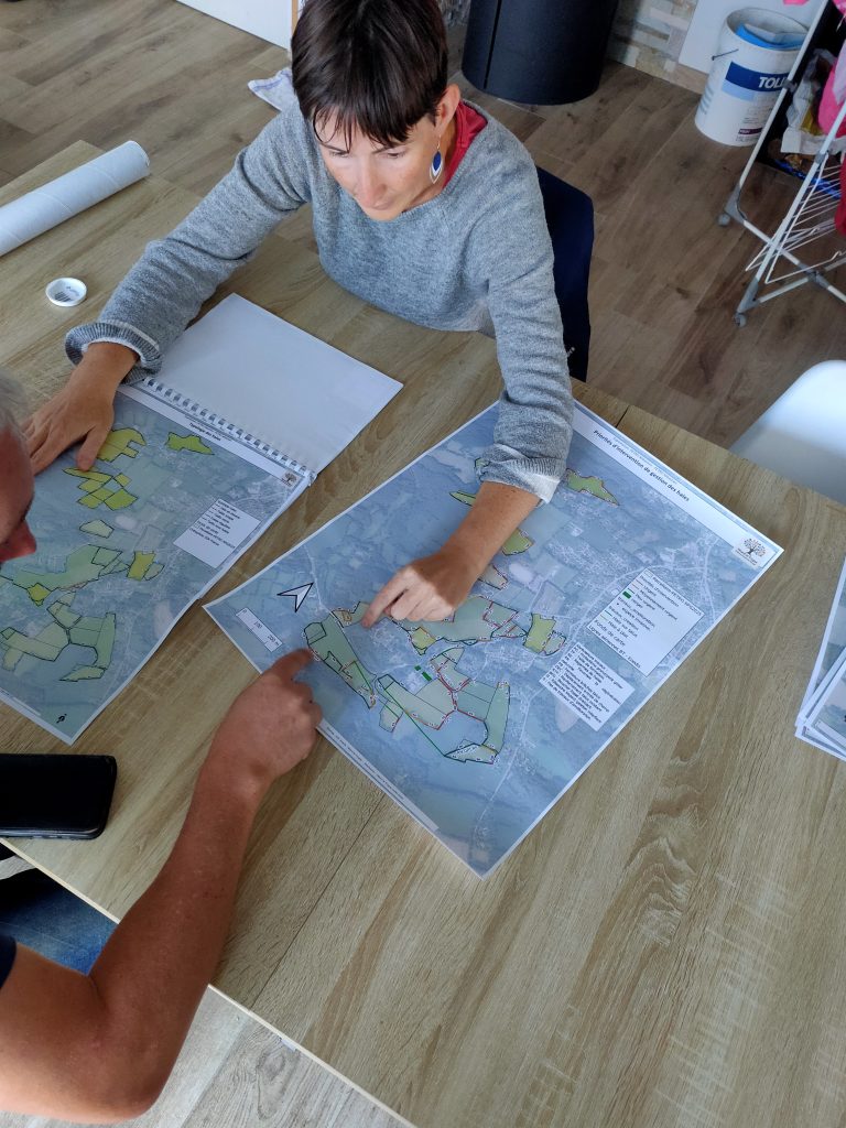 Photo en contre plongée, au premier plan sur une table sont affichée les cartes, une technicienne explique sur plan les priorités de gestion devant l'agriculteur